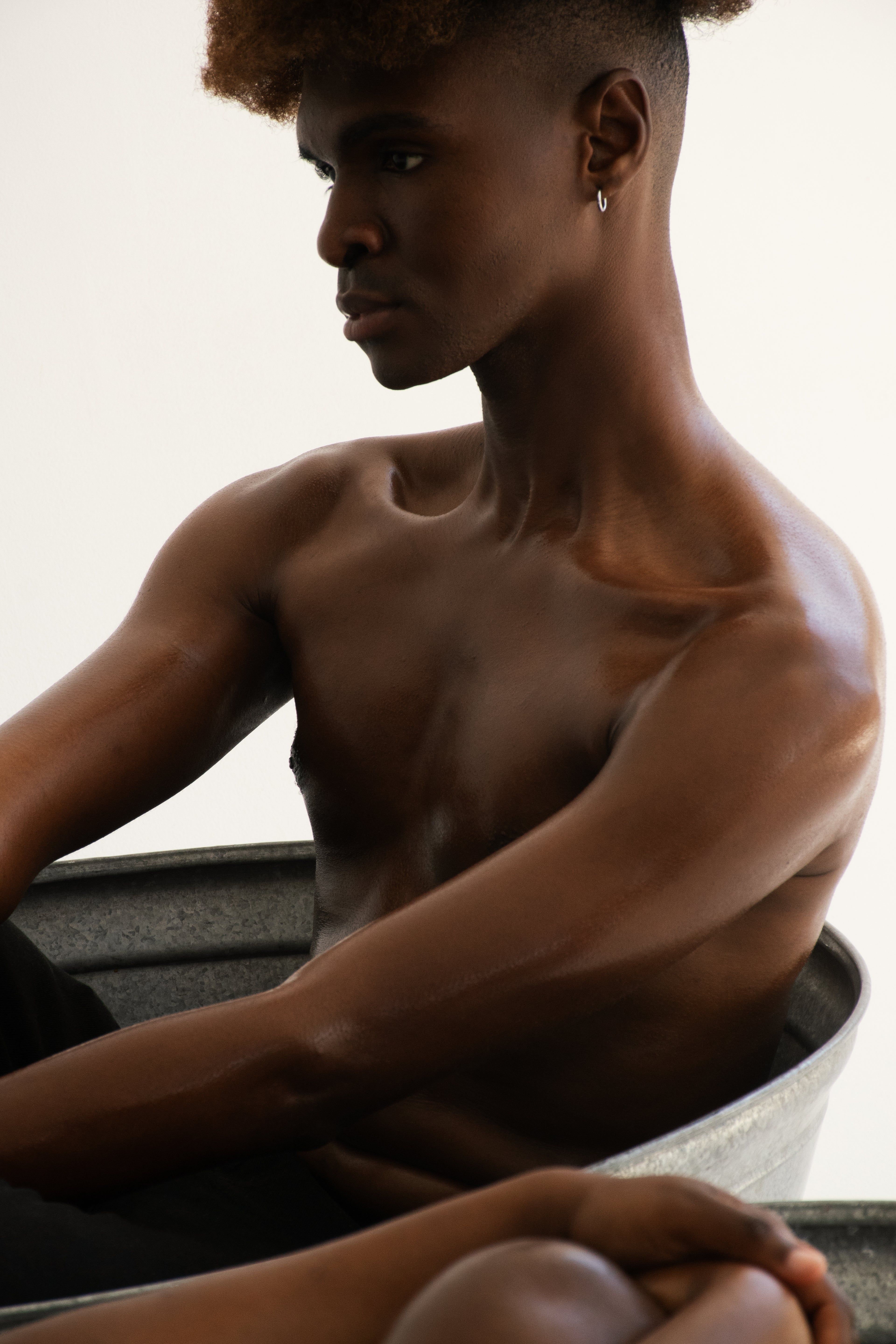 Man sitting shirtless in a metal tub with a neutral background
